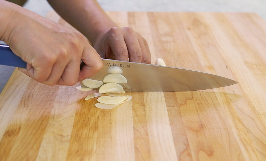 How to cut garlic: Hands use a Misen Chef's Knife to slice garlic