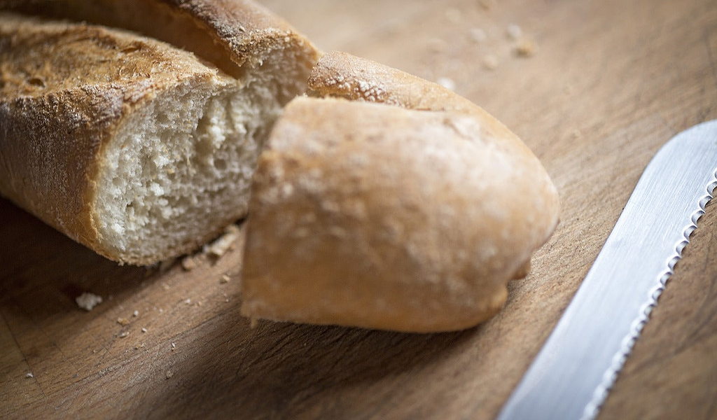 Serrated knife: a bread knife on a cutting board next to a sliced baguette 