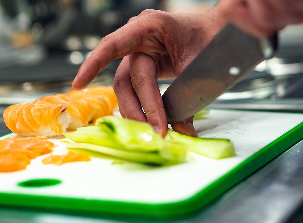 Cutting board material: Hands slice cucumber on a plastic cutting board