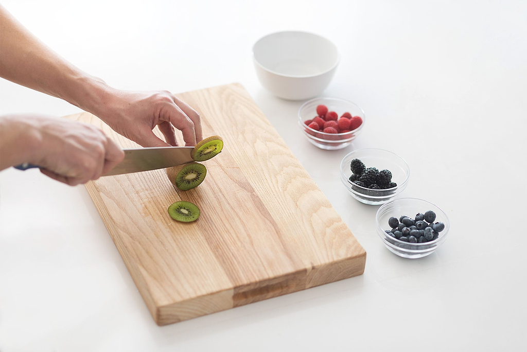 Best wood for cutting board: the Misen ash cutting board with knife slicing kiwi