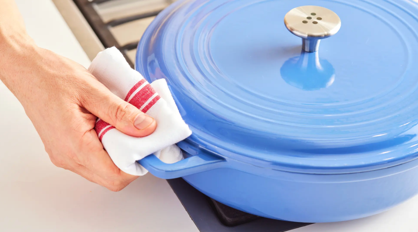 Hand holding blue enameled cast iron dutch oven with kitchen towel on stovetop