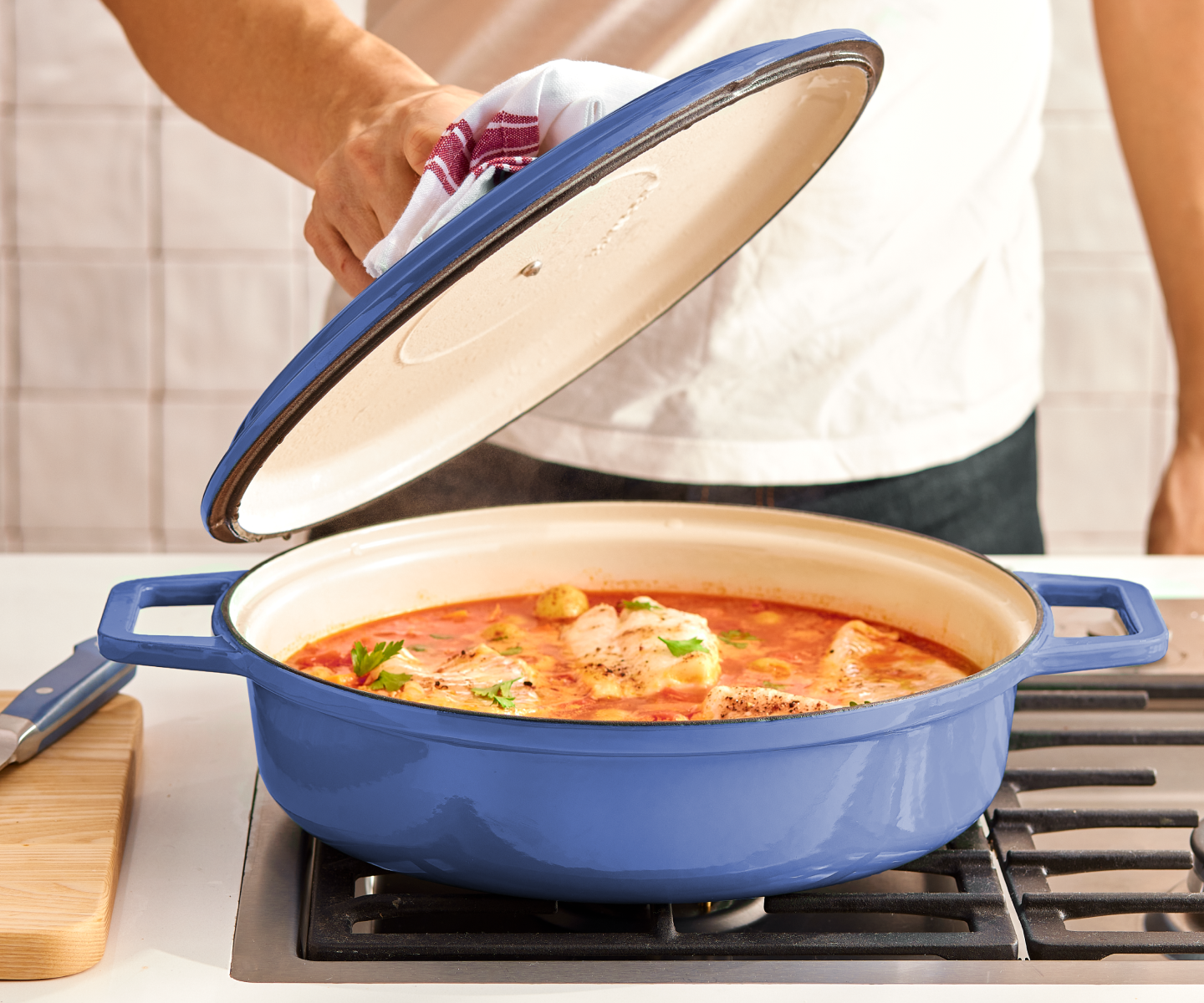 Blue enameled cast iron braiser with fish in tomato sauce on gas stovetop
