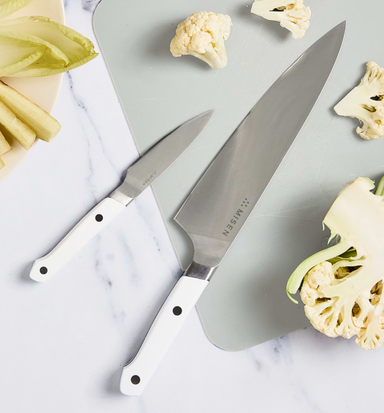 Misen chef's knife and paring knife with white handles on cutting board with cauliflower
