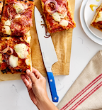 Misen chef's knife with blue handle cutting homemade Detroit-style pizza on wooden board