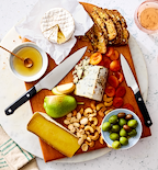 Cheese board with brie, blue cheese, aged cheese, pear, cashews, olives, dried apricots, artisan bread, and honey