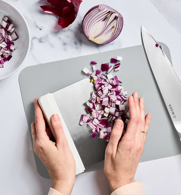 Hands dicing red onion on cutting board with Misen chef knife