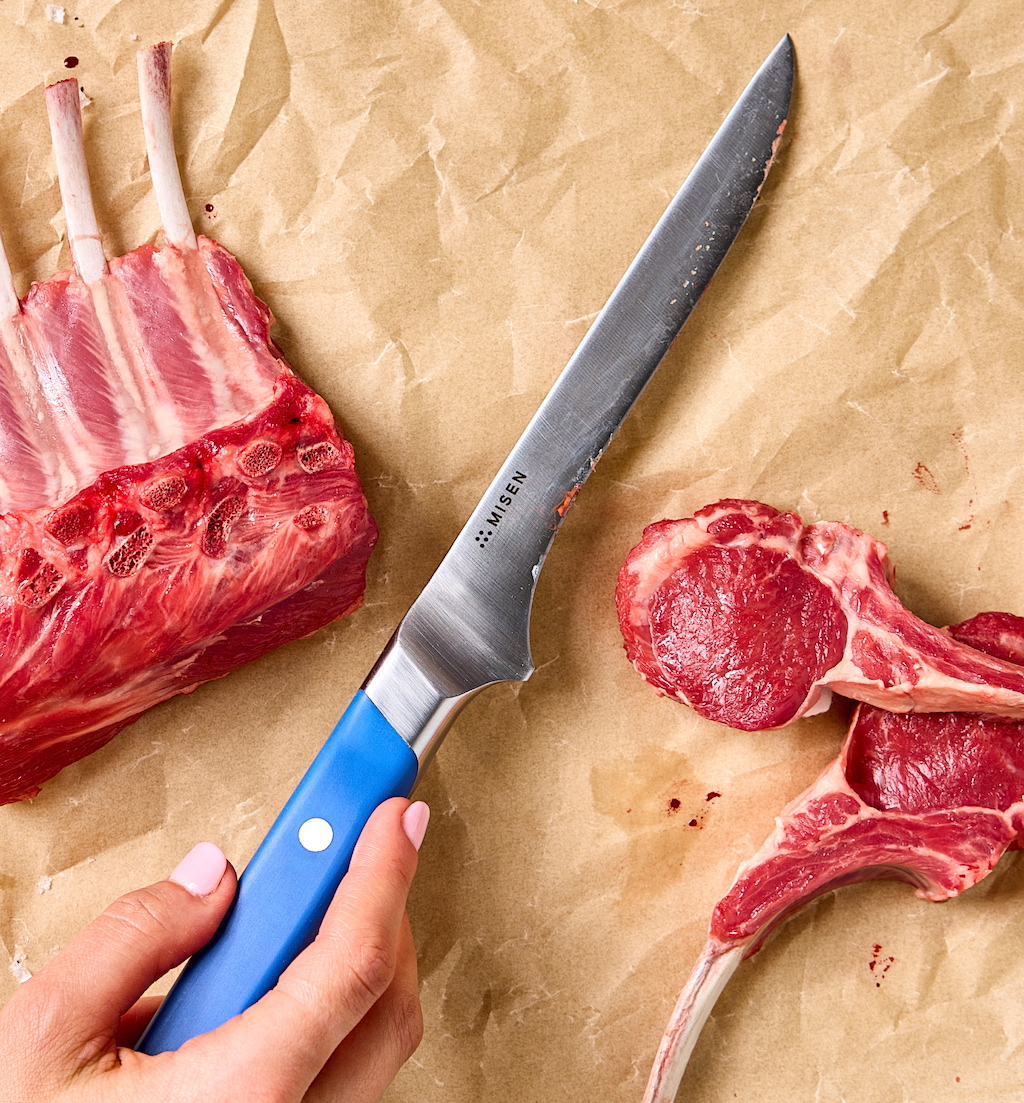 Misen boning knife with blue handle cutting rack of lamb chops on parchment paper