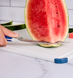 Cutting watermelon rind off with a chef's knife on a white cutting board
