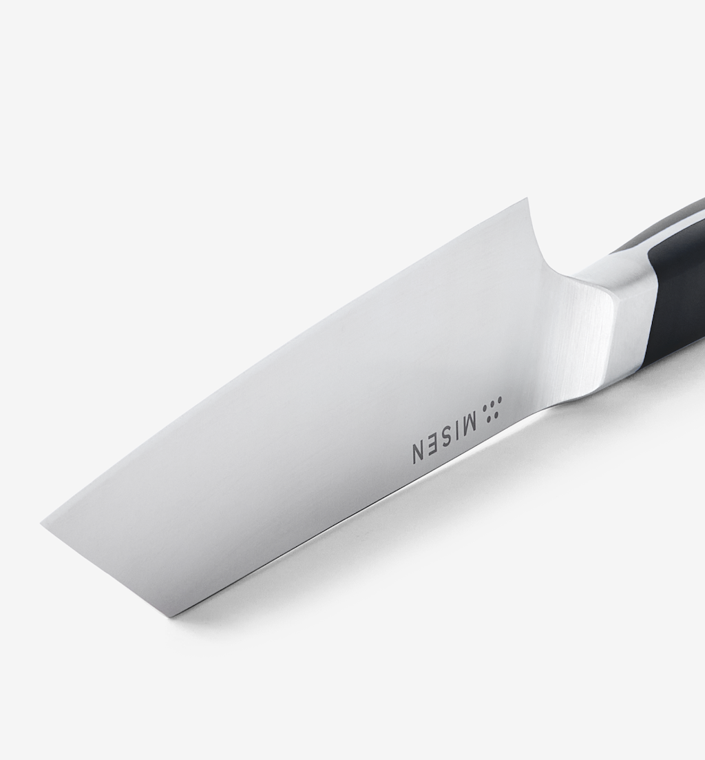 Misen chef's knife blade close-up showing polished stainless steel and bolster