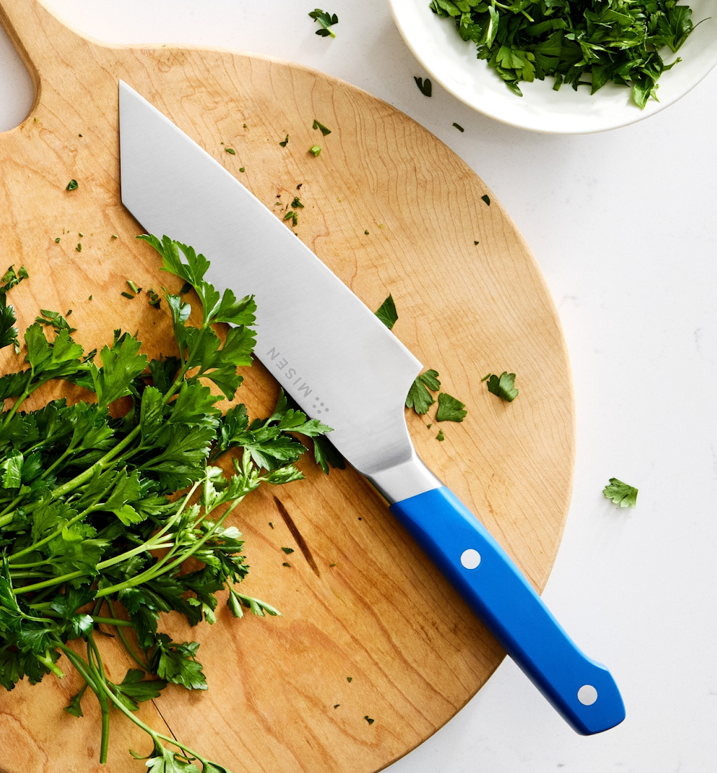 Misen chef's knife with blue handle on wooden cutting board with fresh parsley