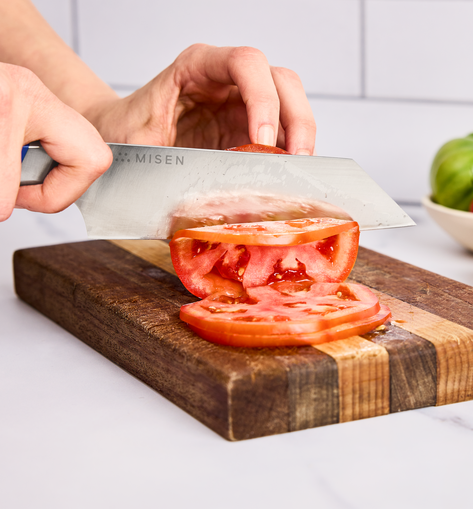 Misen chef's knife slicing a fresh tomato on a wooden cutting board