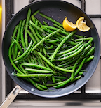 Sautéed green beans with lemon wedges and seasoning in a nonstick skillet