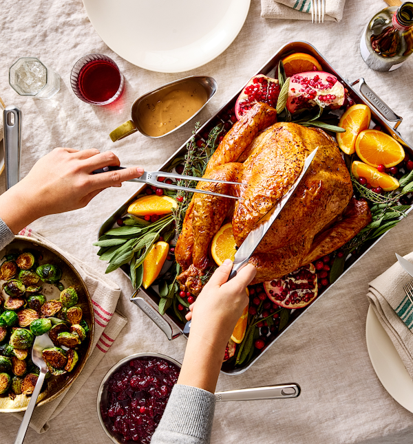 Roasted Thanksgiving turkey on a roasting pan surrounded by oranges, pomegranate, cranberries, and fresh herbs