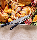 Misen carving knife and fork set beside sliced roast turkey with oranges and pomegranate