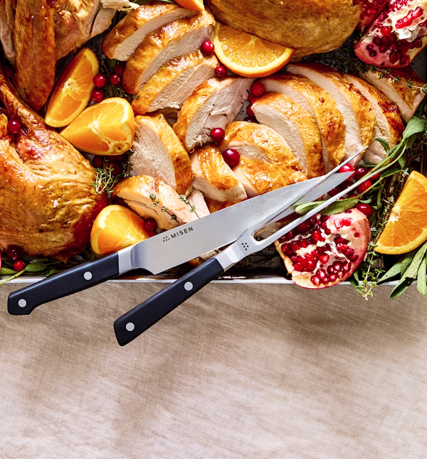 Misen carving knife and fork set beside sliced roast turkey with oranges and pomegranate