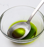 Bright green liquid in glass bowl with stainless steel measuring spoon showing 1 tablespoon and 1 teaspoon markings