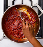 Hand stirring rich tomato sauce in a stainless steel Misen pan on gas stovetop