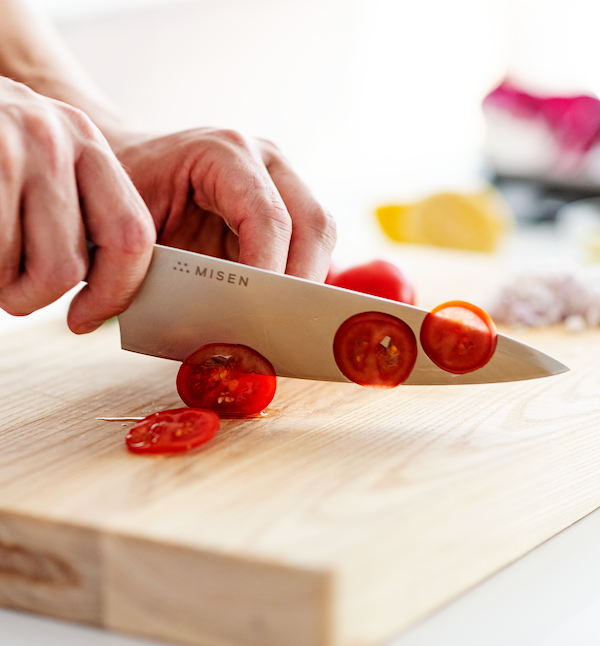 Misen chef's knife slicing cherry tomatoes on a wooden cutting board