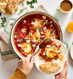 Shakshuka with feta cheese and fresh cilantro served from a green cast iron pan with pita bread
