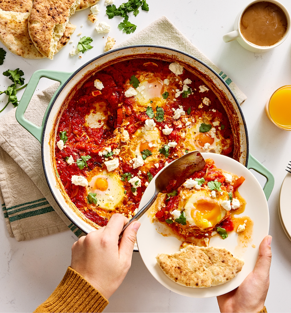 Shakshuka with feta cheese and fresh cilantro served from a green cast iron pan with pita bread