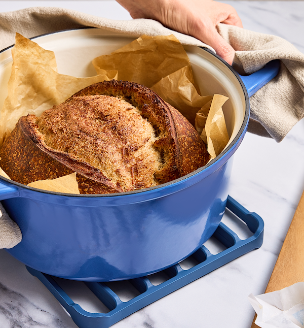 Freshly baked sourdough bread in a blue enameled cast iron Dutch oven lined with parchment paper