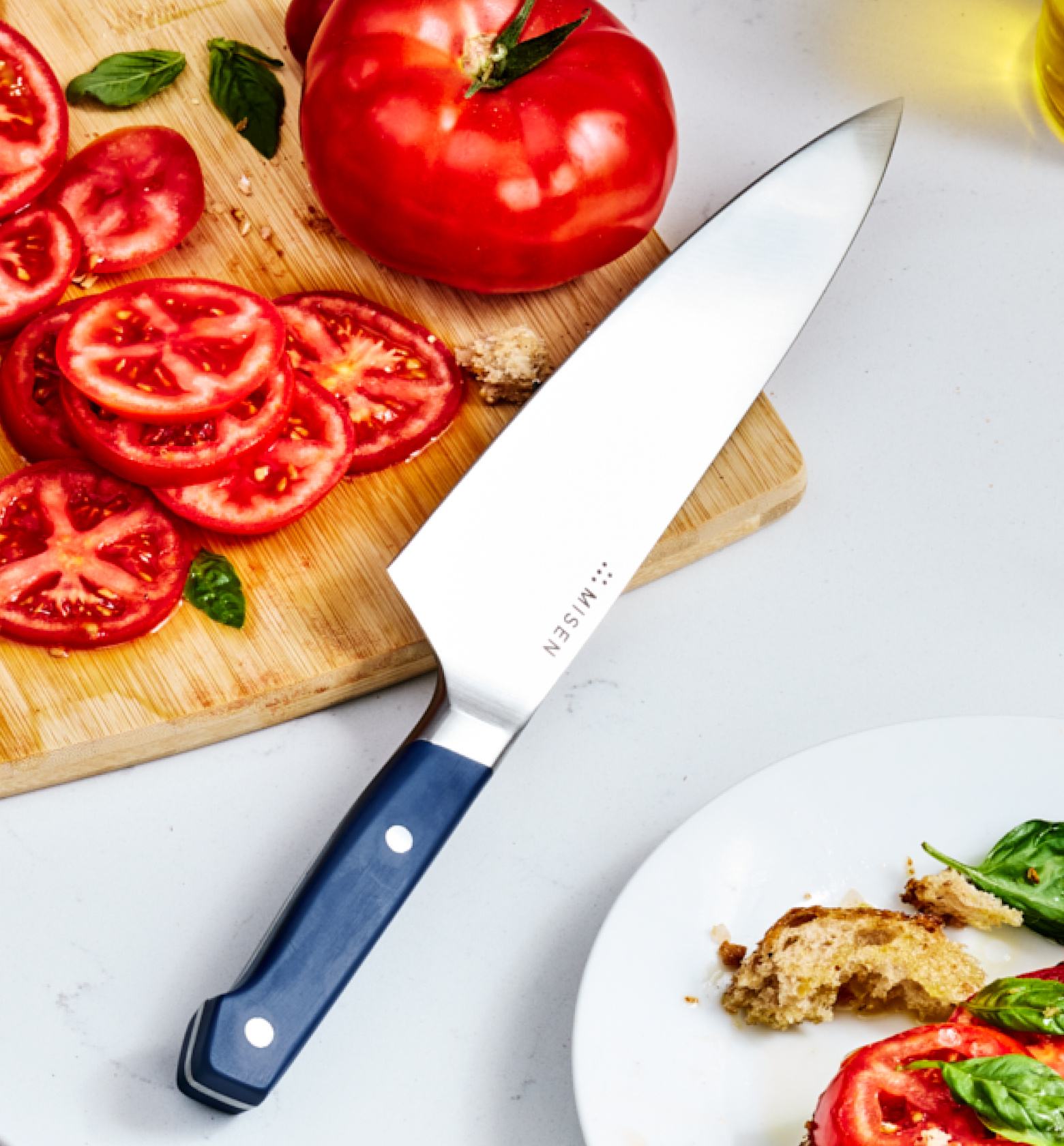 Misen chef's knife with blue handle next to sliced heirloom tomatoes on wooden cutting board