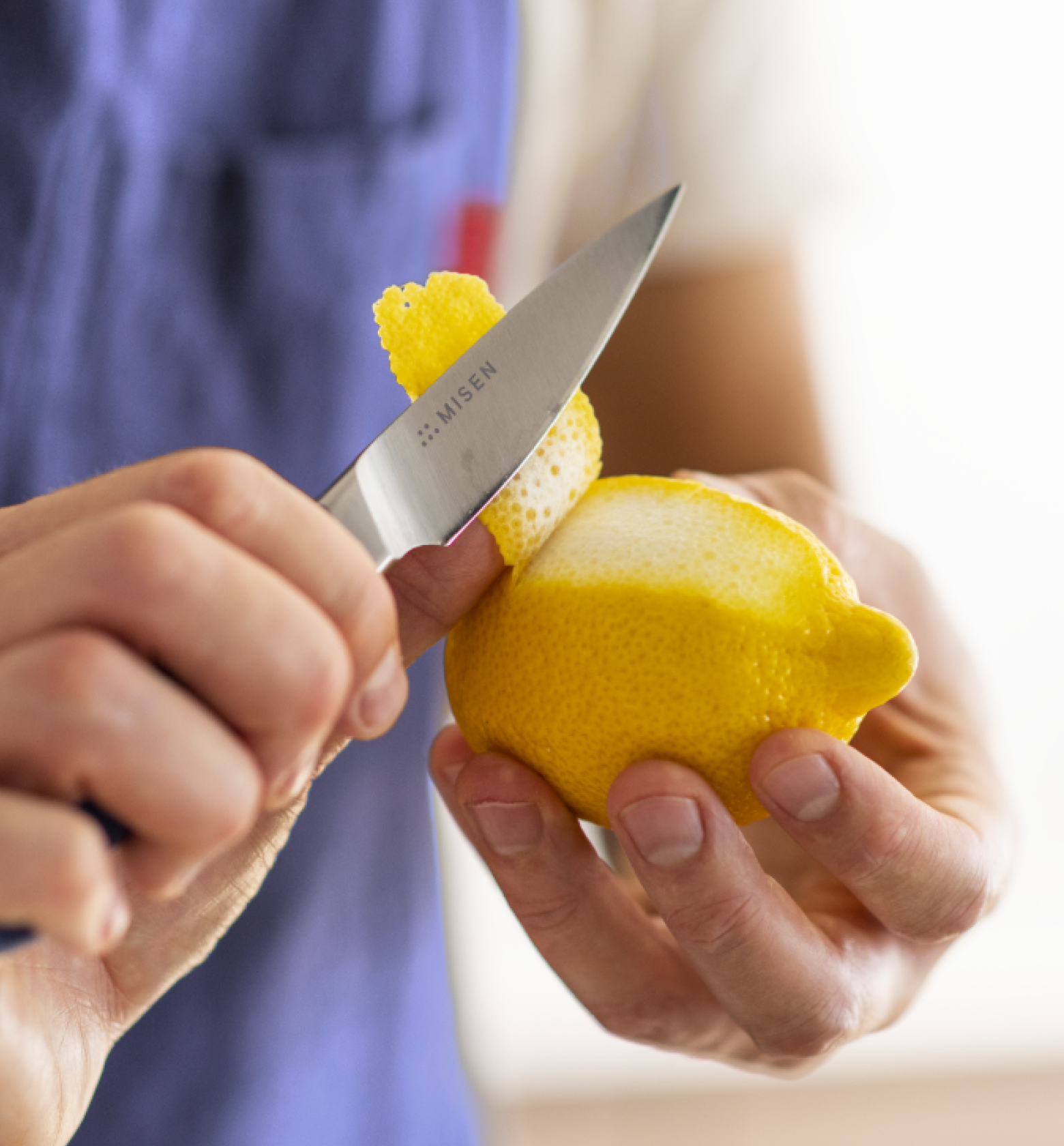 Hands peeling a lemon with a Misen paring knife