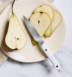 Misen paring knife with white handle beside sliced green pear on cream plate