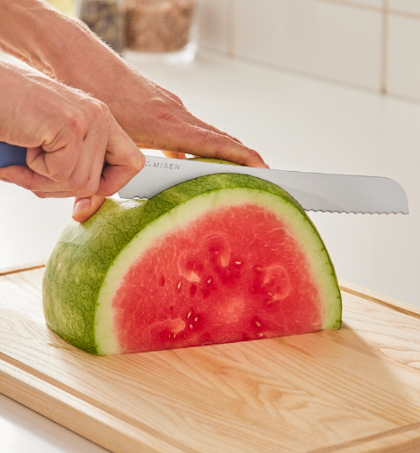 Misen serrated knife slicing a halved watermelon on a wooden cutting board