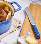 Misen bread knife beside sourdough in blue Dutch oven with butter on cutting board
