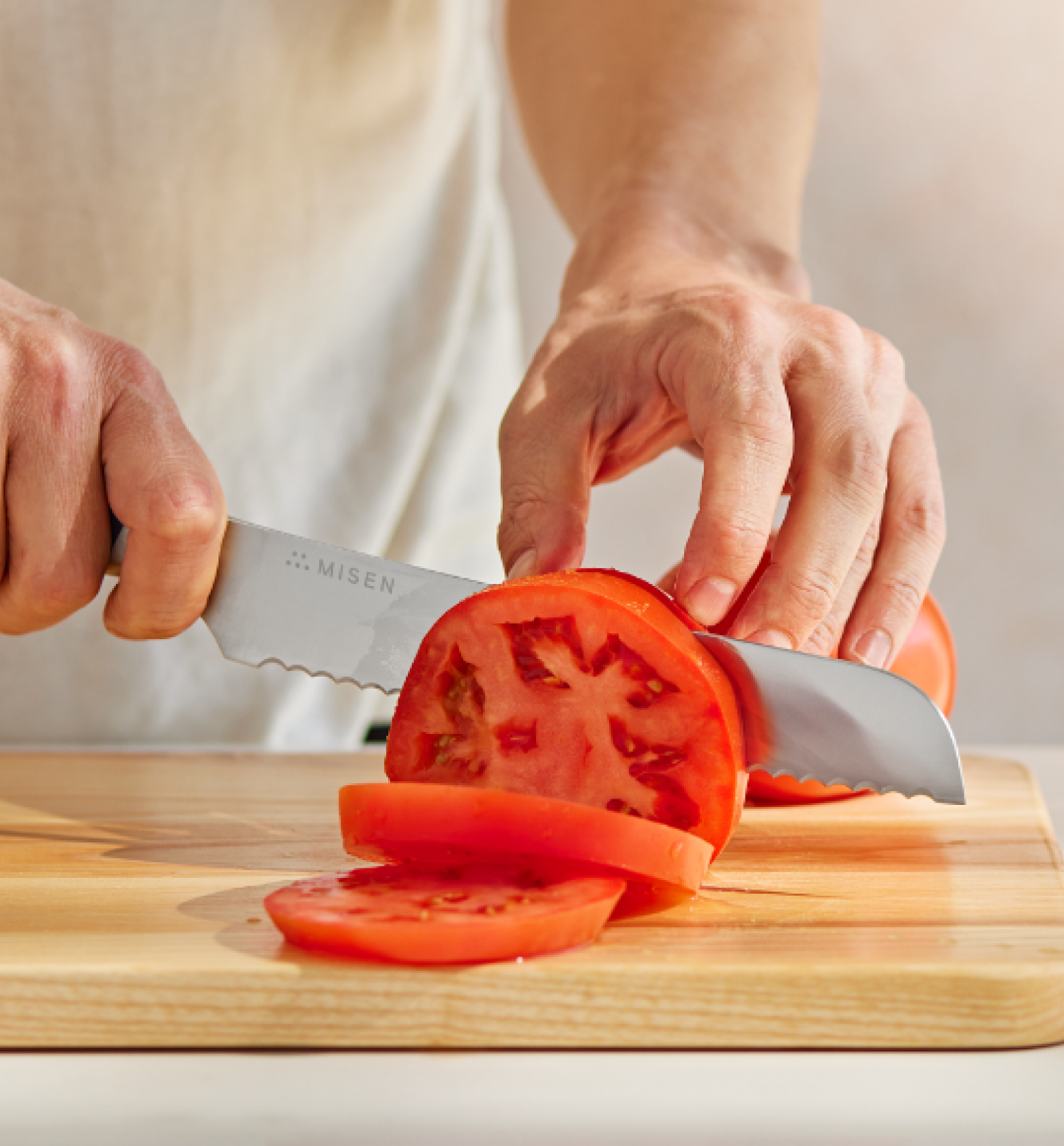 Misen serrated knife slicing fresh tomato on wooden cutting board