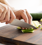 Chef slicing zucchini on wooden cutting board with sharp kitchen knife