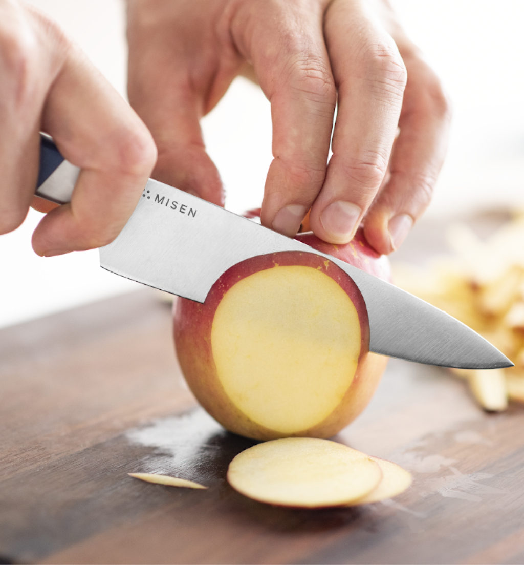 Misen paring knife slicing a fresh red apple on a wooden cutting board