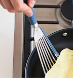 Blue-handled slotted spatula flipping an omelette in a nonstick frying pan on a gas stove
