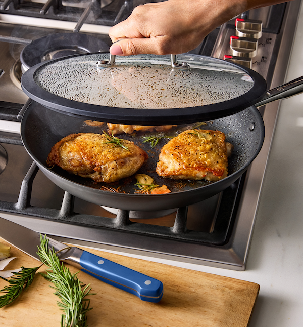 Golden brown pan-seared chicken thighs cooking in nonstick skillet with rosemary and garlic on gas stove