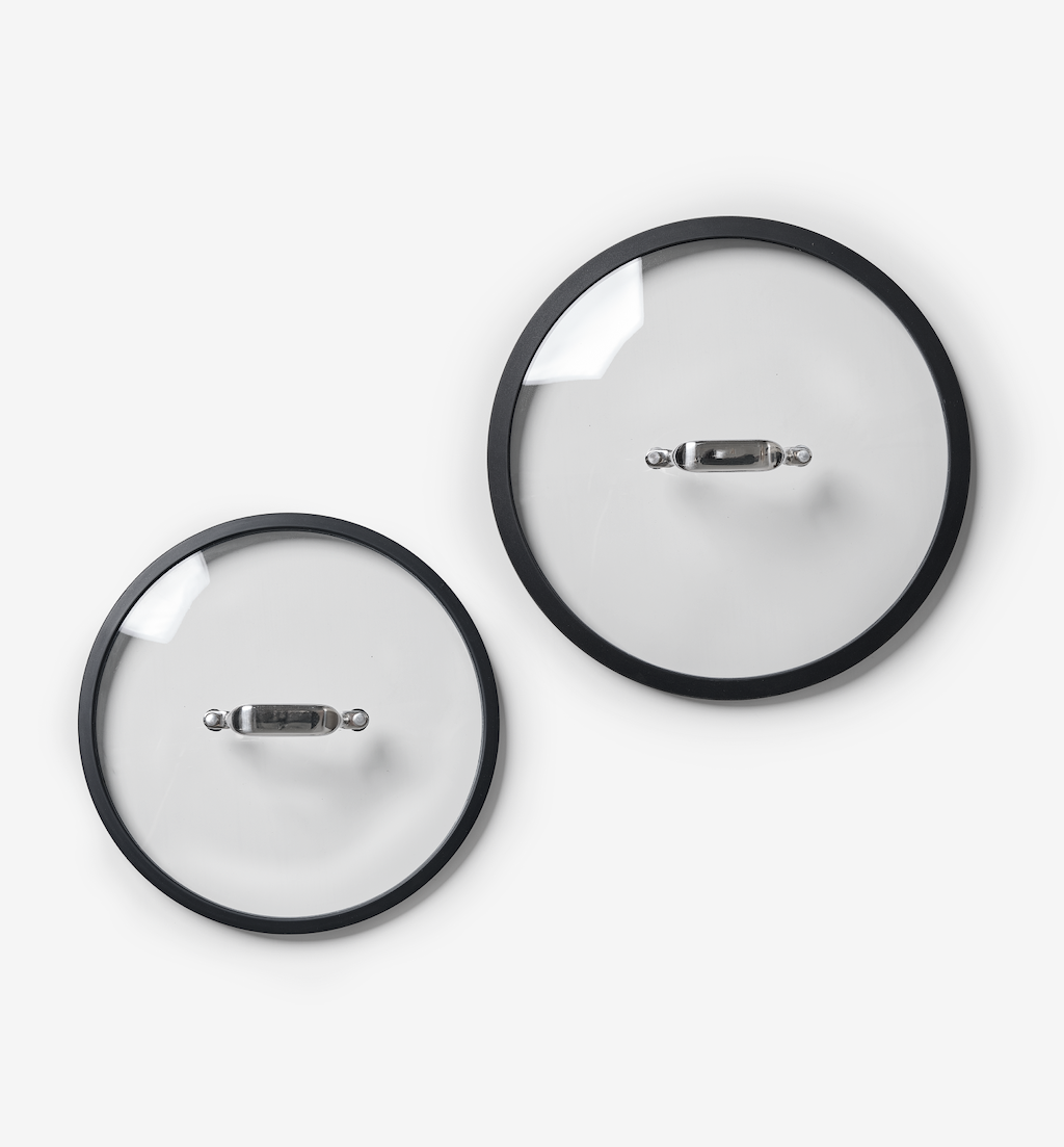 Two glass pot lids with stainless steel handles and black silicone rims, different sizes