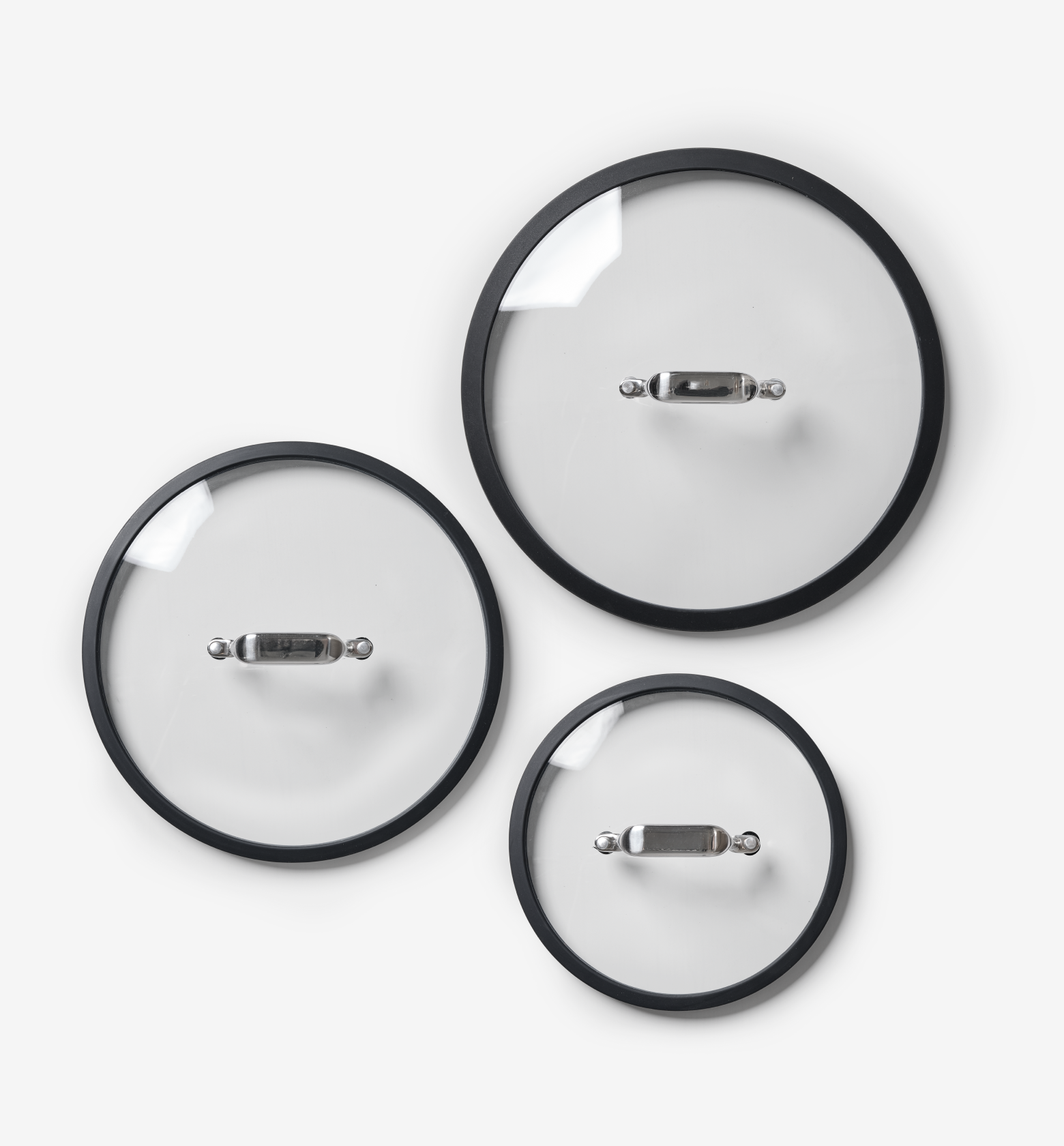 Set of three glass cookware lids with black rims and stainless steel handles in small, medium, and large sizes