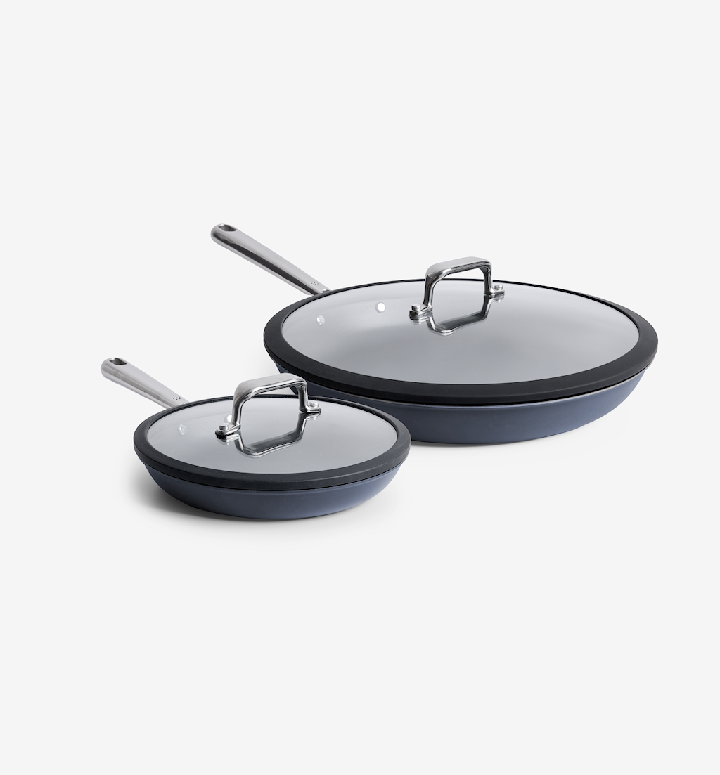 Two dark gray nonstick frying pans with glass lids and stainless steel handles, small and large sizes