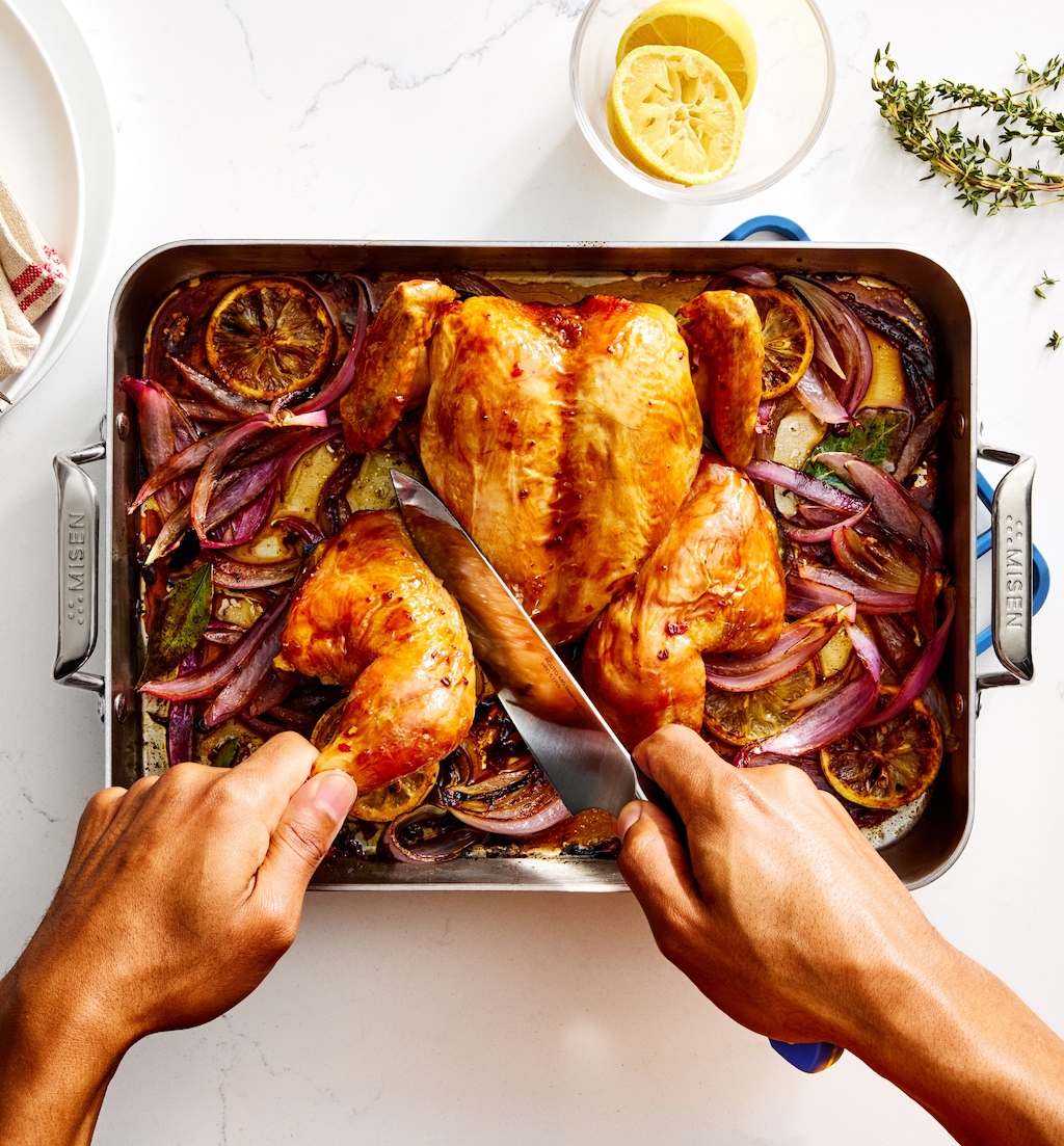 Hands carving roasted whole chicken with lemon and red onion in Misen roasting pan