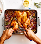 Hands carving roasted whole chicken with lemon and red onion in Misen roasting pan