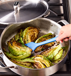 Sautéed cabbage wedges with fresh herbs in stainless steel pan on gas stove