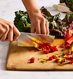 Misen chef's knife chopping colorful rainbow chard stems on wooden cutting board