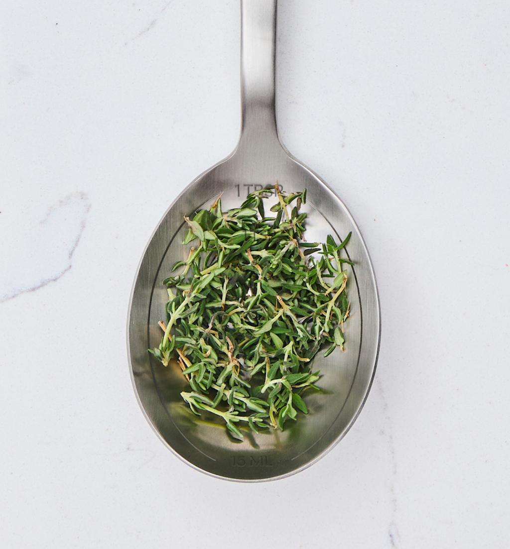 One tablespoon of fresh thyme leaves on stainless steel measuring spoon