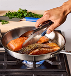 Pan-seared salmon fillets cooking in stainless steel skillet on gas stove