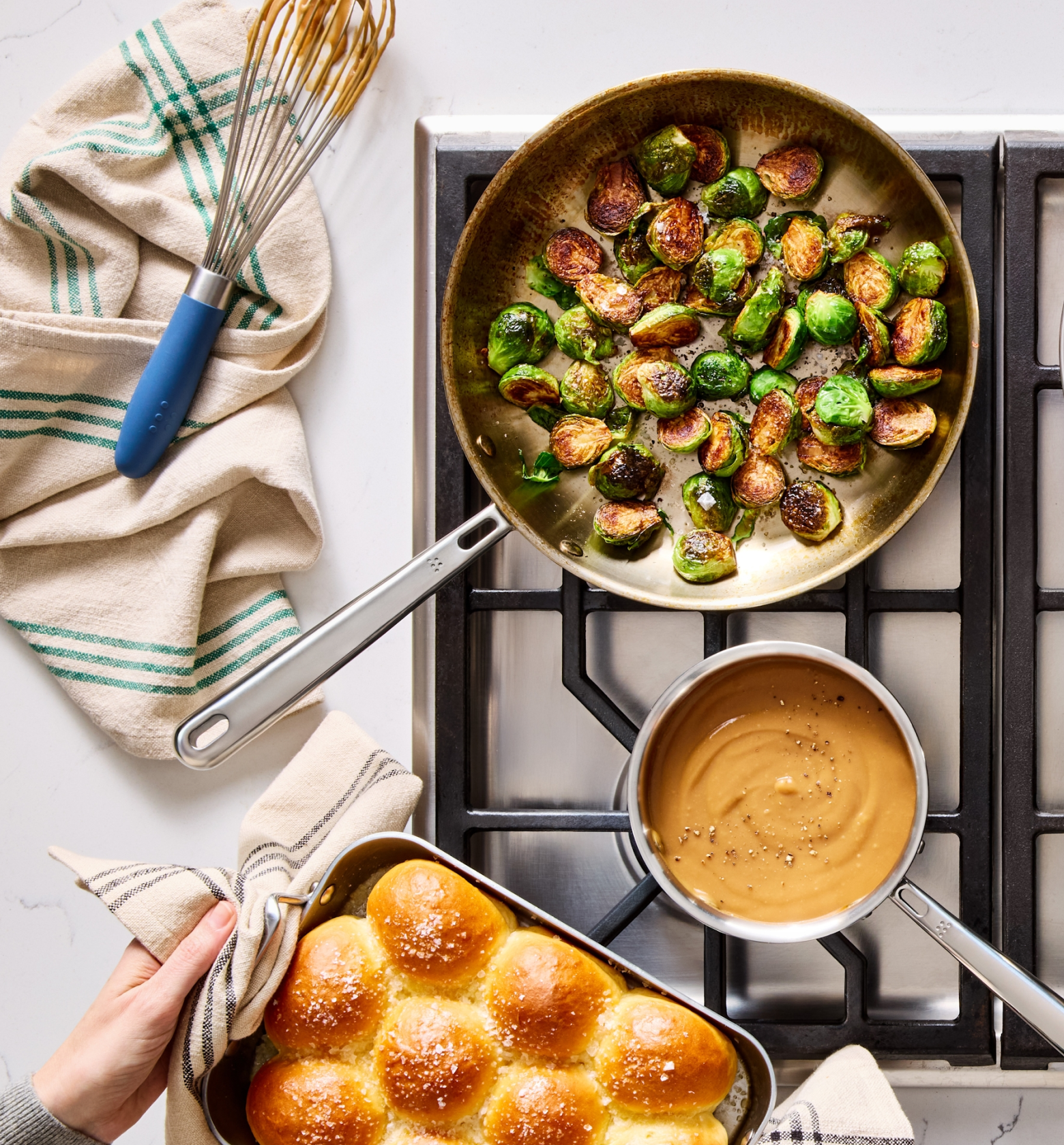 Sautéed Brussels sprouts in skillet with creamy sauce and dinner rolls on stovetop