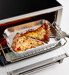 Cheese pizza slices reheating in a toaster oven on a silver baking pan with a spatula