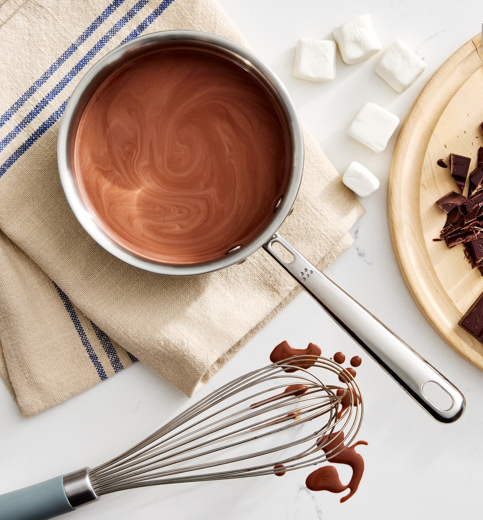 Homemade hot chocolate in saucepan with marshmallows, chopped dark chocolate, and whisk