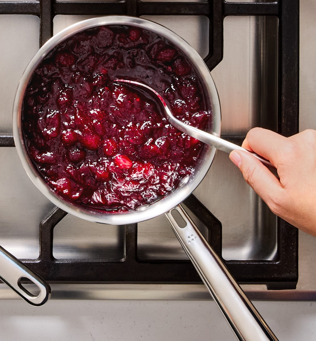 Homemade cranberry sauce simmering in stainless steel saucepan on gas stove