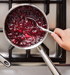 Homemade cranberry sauce simmering in stainless steel saucepan on gas stove