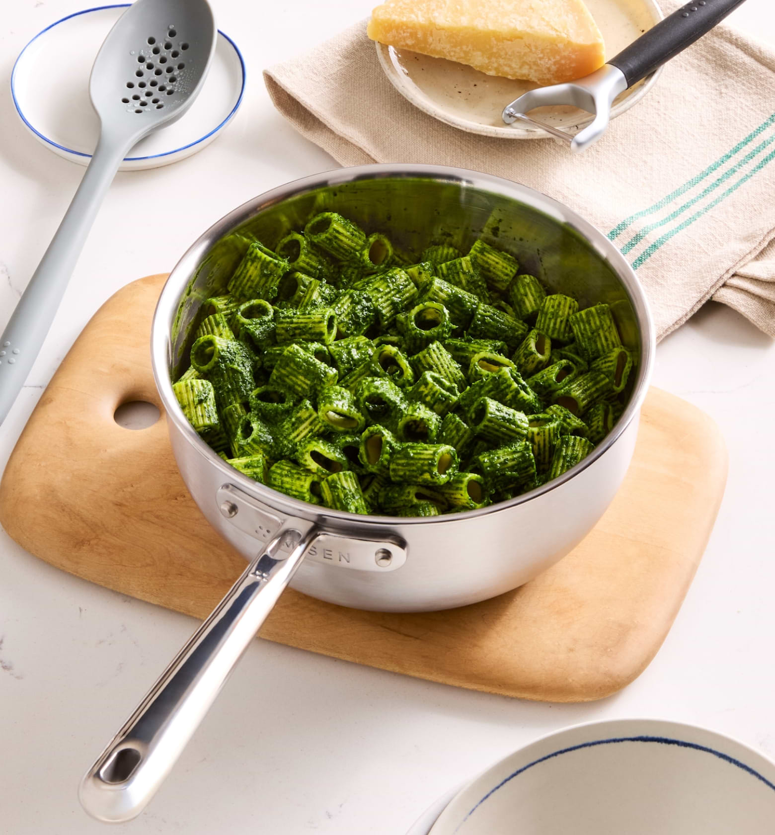 Rigatoni pasta with green pesto sauce in stainless steel saucepan on wooden cutting board